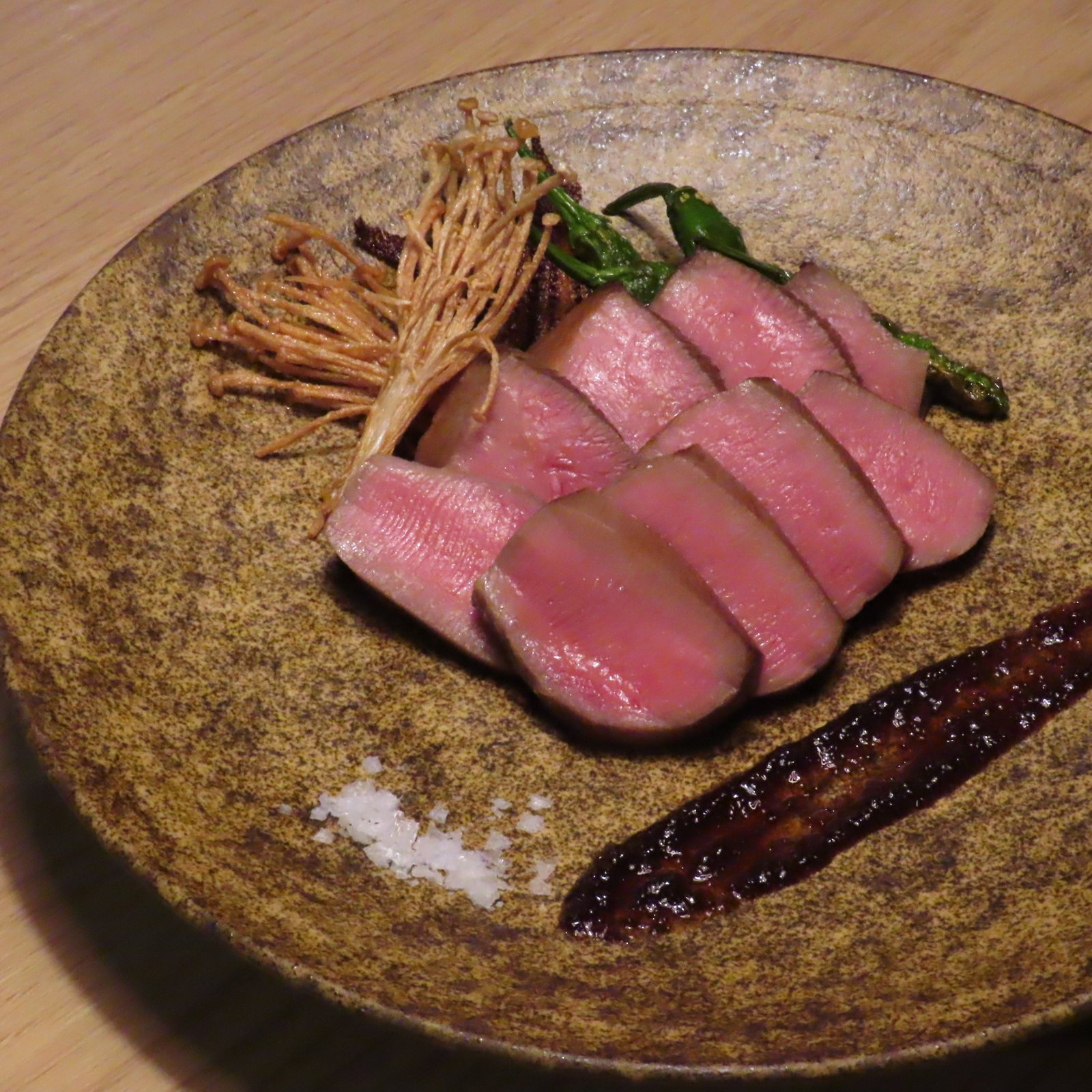 厚切りの焼いた肉に黒いソースと揚げたえのき