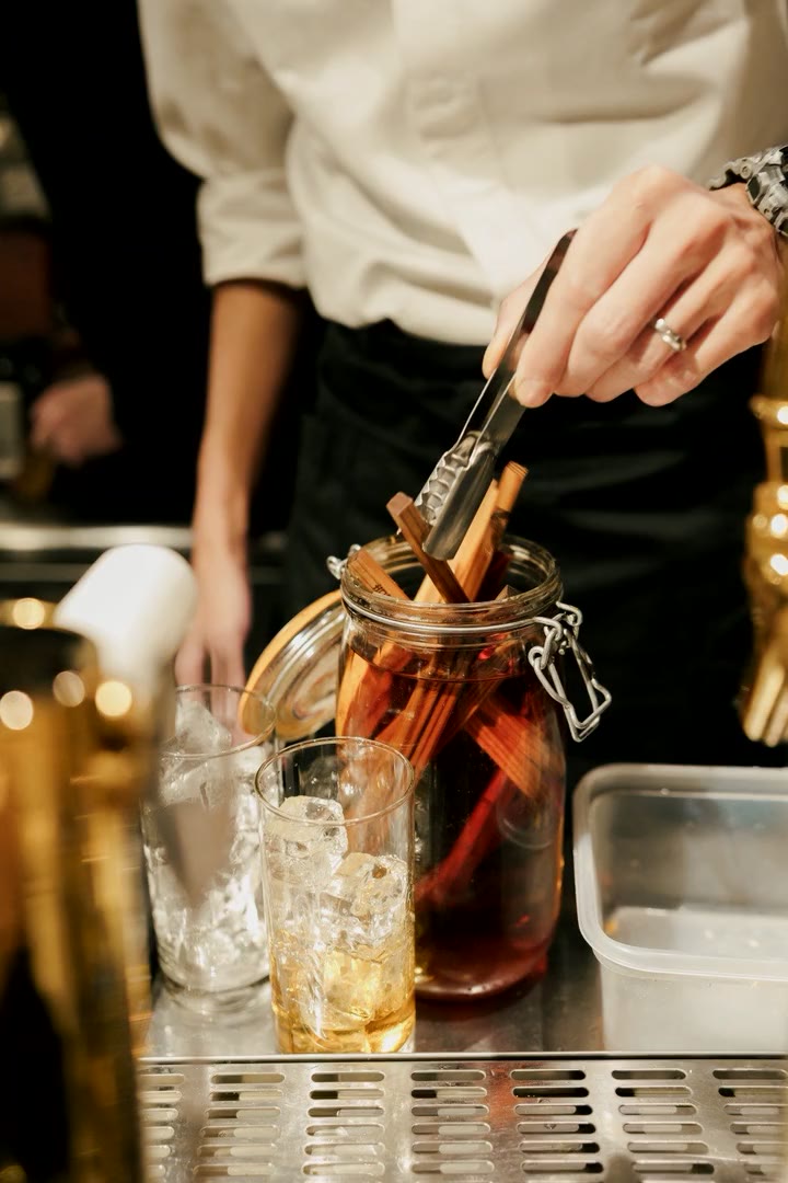 カウンターで木片を漬けた瓶から酒を注ぐ手元